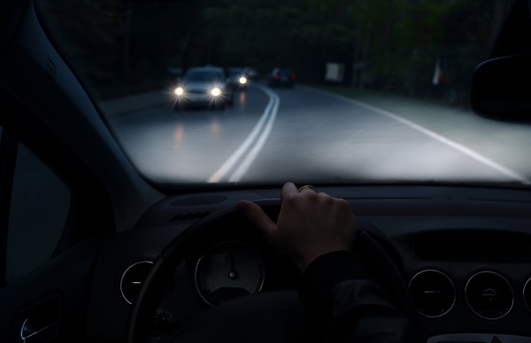 POV, driving at night on a dark road with oncoming cars in the opposite lane, headlights illuminated.