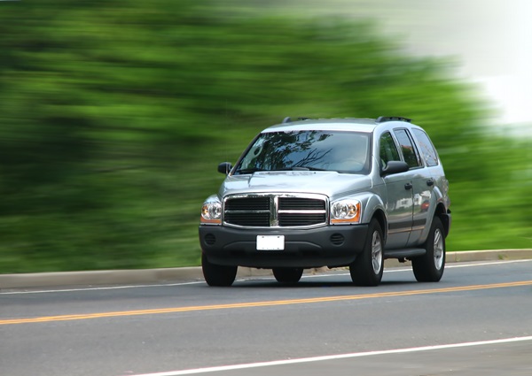 A grey SUV speeding down the road with motion blur and green bushes in the background.